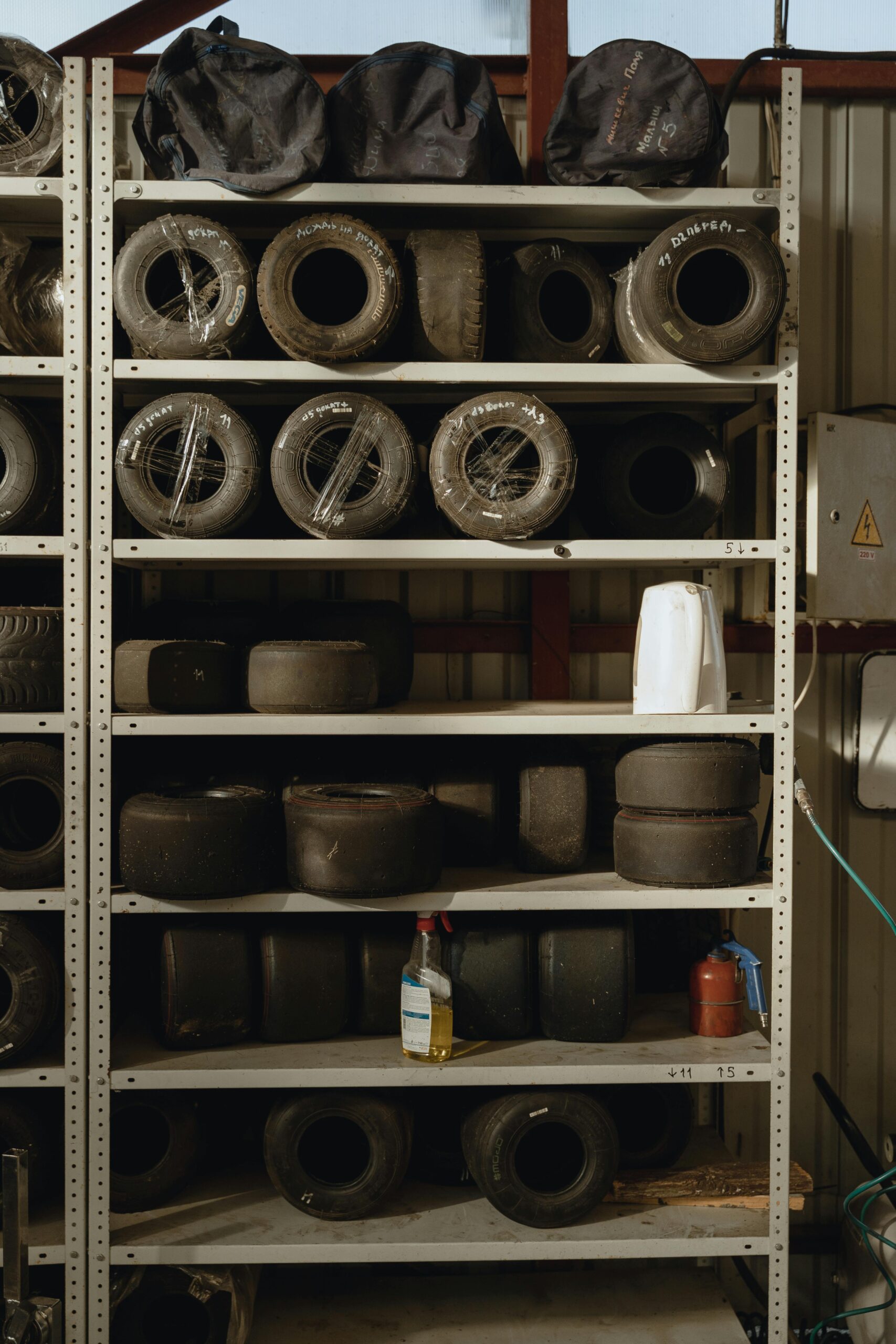 Shelving unit with various sizes of racing or go-kart tires stored in a garage or workshop.